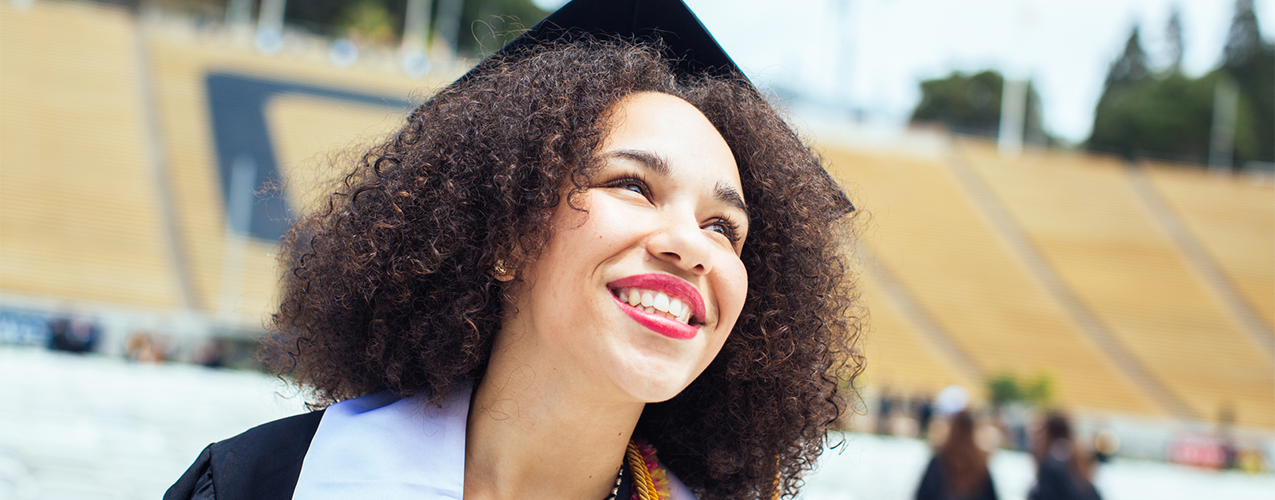 A UC Berkeley student wearing graduation robes looks to the sky.