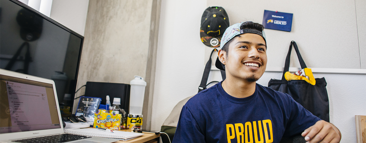 UC Merced student sits at a desk in a dorm room.