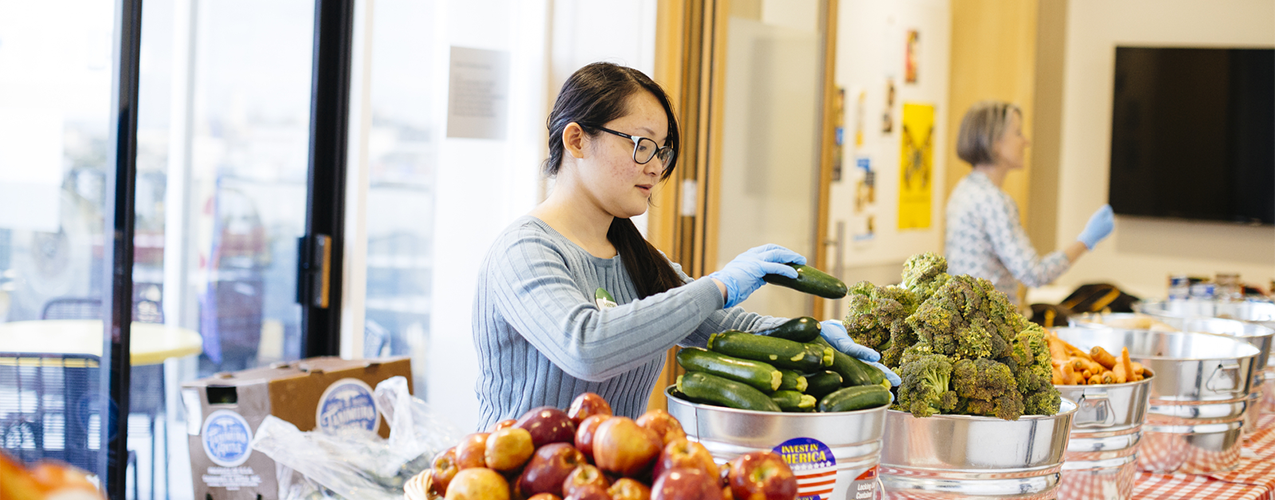 A food bank volunteer stacks a zucchini in a bucket.